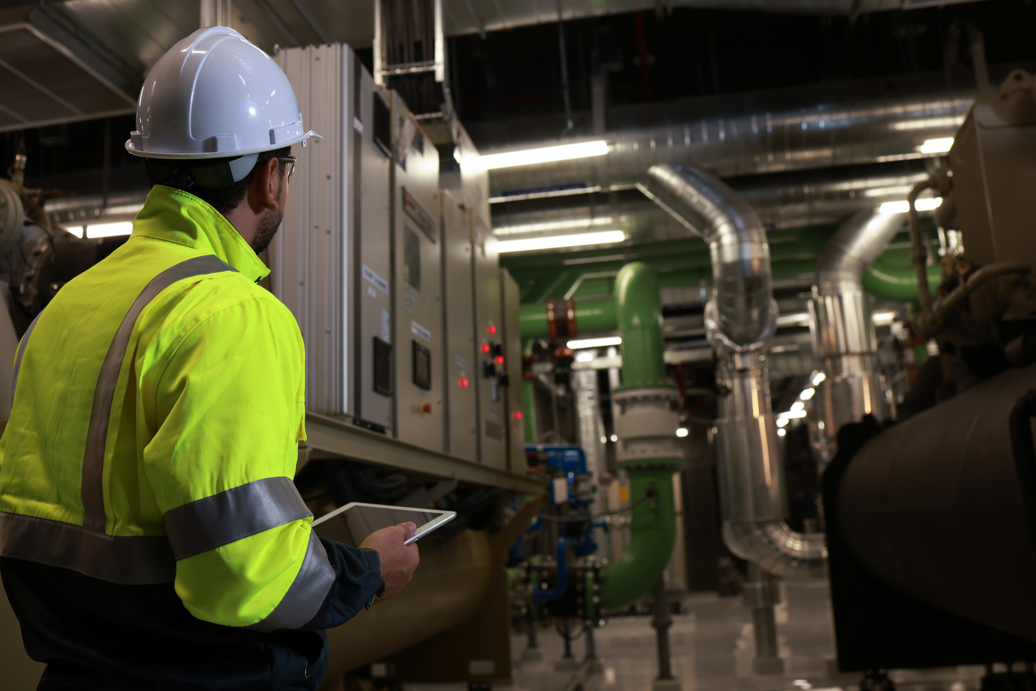 Facility technician inspecting critical infrastructure equipment in a mechanical and power systems room.