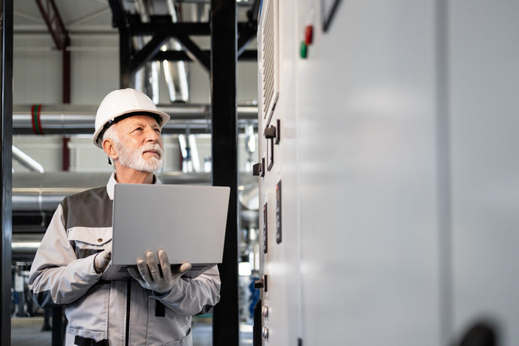 Facility engineer inspecting mission critical power equipment with a laptop in an electrical room.