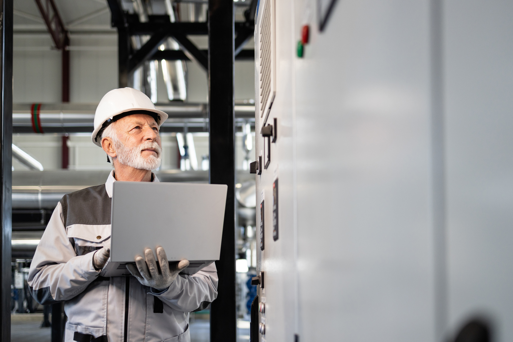 Facility engineer inspecting mission critical power equipment with a laptop in an electrical room.